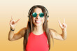 © Westend61 - Young woman with headphones gesturing horn sign over yellow background