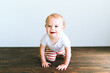 © Cavan Images - A baby boy crawls across a dark wood floor in front of a white wall