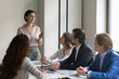 © fizkes - Mature female boss talking to employees on office meeting, standing at table, speaking, instructing business team, explaining task, motivating for teamwork. Corporate teacher training new workers