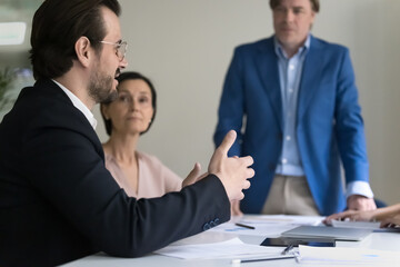 Wall Mural - Engaged handsome business employee man talking to colleagues on office meeting with CEO, leader, boss, offering idea, speaking, brainstorming with group. Close up side view