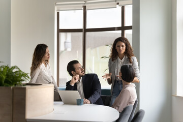 Canvas Print - Diverse team meeting at work desk with laptop, listening to serious young female boss. Business leader woman instructing group, telling plan, explaining project tasks, presenting ideas