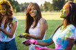 Multiethnic group of happy playful friends playing and having fun with holi colorful powder at the park
