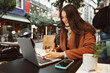 © fotofabrika - Young woman working with her laptop sitting at the table in the street