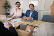 © fizkes - Cheerful mature couple of business colleagues discussing marketing strategy on office meeting, holding paper statistic reports, talking, listening to colleagues, brainstorming, smiling, laughing