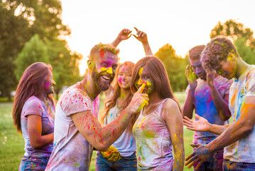 Multiethnic group of happy playful friends playing and having fun with holi colorful powder at the park