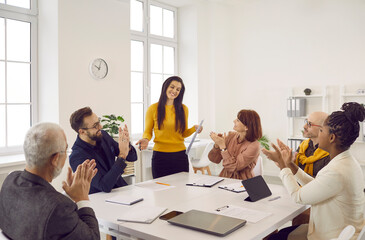 Woman receives ovation she deserves at work meeting for successful presentation on increasing sales from multiethnic team of happy positive coworkers sitting at table in modern white office boardroom