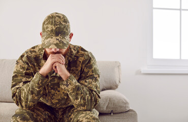 Serious anxious and nervous military man suffers from depression while sitting alone at home. Pensive man in military uniform sitting on sofa propping his head with his hands. PTSD concept.