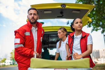 Wall Mural - paramedics with a stretcher near an ambulance. Paramedics in uniform taking stretcher out the ambulance car