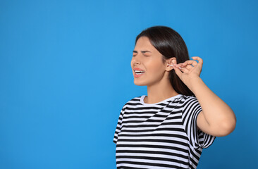 Sticker - Young woman cleaning ear with cotton swab on light blue background, space for text