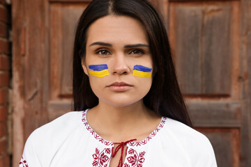 Wall Mural - Young beautiful woman with drawings of Ukrainian flag on face near wooden door