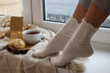 Woman in warm socks relaxing on window sill at home, closeup