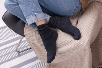 Wall Mural - Woman in warm socks sitting on armchair at home, closeup