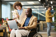 © pressmaster - Young female employee with notepads looking at screen of laptop on knees of African American male colleague sitting in wheelchair