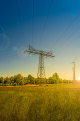 Wall Mural - Beautiful farm landscape and industrial high voltage power line pylons and wind turbines farm at sunset warm colors and direct sun light with lens flare and sun rays in Germany