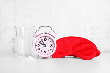 Wall Mural - Red sleep mask, glass of water, pills and alarm clock on white table