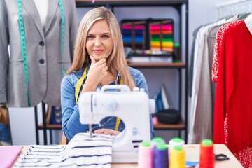 Canvas Print - Blonde woman dressmaker designer using sew machine looking confident at the camera smiling with crossed arms and hand raised on chin. thinking positive.