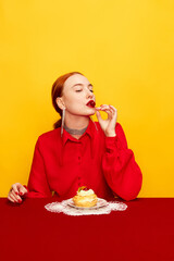 Wall Mural - Beautiful young girl in red shirt tasting delicious cake with cream filling on yellow studio background. Food pop art photography. Complementary colors. Concept of art, beauty, food. Copy space for ad