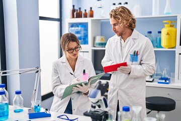 Wall Mural - Man and woman wearing scientist uniform writing on notebook using touchpad at laboratory