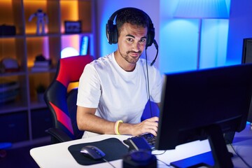 Poster - Young hispanic man streamer smiling confident sitting on table at gaming room