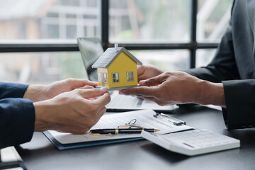 Wall Mural - Young Asian real estate agent, and insurance salesman handing over a sample house to a client after signing the sale at the office.