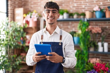 Young hispanic man florist smiling confident using touchpad at florist