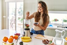 Young Beautiful Hispanic Woman Preparing Vegetable Smoothie With Blender At The Kitchen