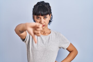 Sticker - Young hispanic woman wearing casual t shirt over blue background looking unhappy and angry showing rejection and negative with thumbs down gesture. bad expression.