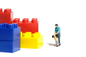 Miniature people toy figure photography. Kids want to play building brick. A father and son walking in front of colorful brick set. Isolated white background