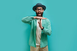 Fototapeta  - Young bearded hipster guy showing time out tired from work. Indoor studio shot against a blue background.