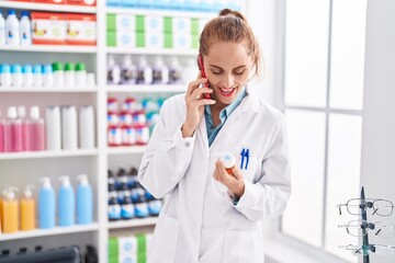 Canvas Print - Young beautiful hispanic woman pharmacist holding pills bottle talking on smartphone at pharmacy