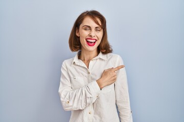 Poster - Young beautiful woman standing casual over blue background cheerful with a smile of face pointing with hand and finger up to the side with happy and natural expression on face