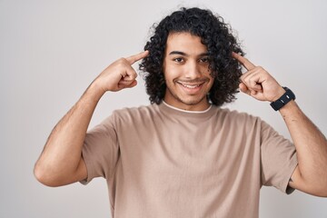 Wall Mural - Hispanic man with curly hair standing over white background smiling pointing to head with both hands finger, great idea or thought, good memory