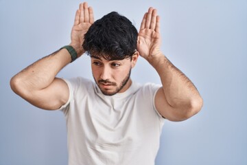 Sticker - Hispanic man with beard standing over white background doing bunny ears gesture with hands palms looking cynical and skeptical. easter rabbit concept.