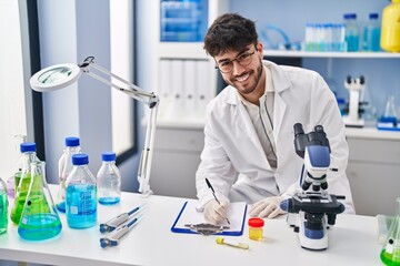 Wall Mural - Young hispanic man scientist writing on document holding urine test tube at laboratory