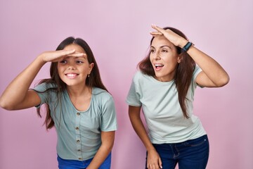 Canvas Print - Young mother and daughter standing over pink background very happy and smiling looking far away with hand over head. searching concept.