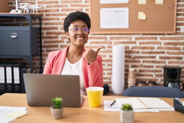 Poster - Young african american woman working at the office wearing glasses pointing thumb up to the side smiling happy with open mouth