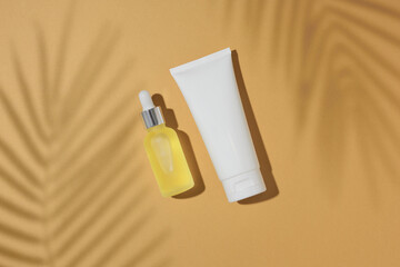 Wall Mural - Sunscreen cosmetic concept. Top view photo of cosmetic bottle, dropper bottle and tropical leaves shadow on sandy background. Flat lay cosmetics mockup idea.