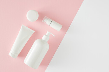 Wall Mural - Skincare products concept. Top view photo of cosmetic tubes without label, pump bottles, cream jars on pastel pink and white background with empty space. Flat lay cosmetics mockup idea.