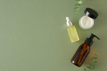 Wall Mural - Organic skincare concept. Top view photo of amber pump bottle, dropper bottle, cream jar and eucalyptus leaves on pastel green background with empty space. Flat lay cosmetics mockup idea.