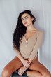 © dmitriisimakov - a brunette woman in a bodysuit sits against a white wall