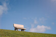 A low-angle view of concrete bench on a grassy hill with blue sky behind