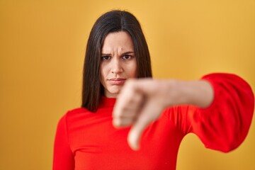 Sticker - Young hispanic woman standing over yellow background looking unhappy and angry showing rejection and negative with thumbs down gesture. bad expression.