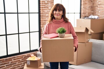 Canvas Print - Middle age hispanic woman moving to a new home holding cardboard box relaxed with serious expression on face. simple and natural looking at the camera.