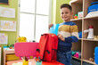 © Krakenimages.com - Adorable hispanic boy student holding book of backpack at kindergarten
