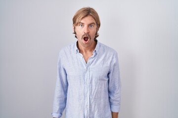 Sticker - Caucasian man with mustache standing over white background in shock face, looking skeptical and sarcastic, surprised with open mouth