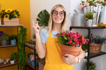 Sticker - Young caucasian woman working at florist shop holding plant smiling happy pointing with hand and finger to the side