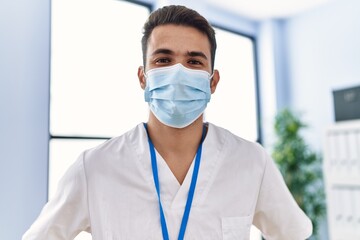 Sticker - Young hispanic man wearing physiotherapist uniform and medical mask at clinic