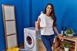 © Krakenimages.com - Young hispanic woman smiling confident holding detergent bottle at laundry room