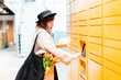 © okrasiuk - Fashion woman with box using modern postal automatic mail terminal with self service device for pickup or refund an order. Electronic locker for storing parcels. Online shopping. Selective focus