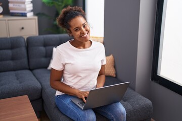 Poster - African american woman using laptop sitting on sofa at home